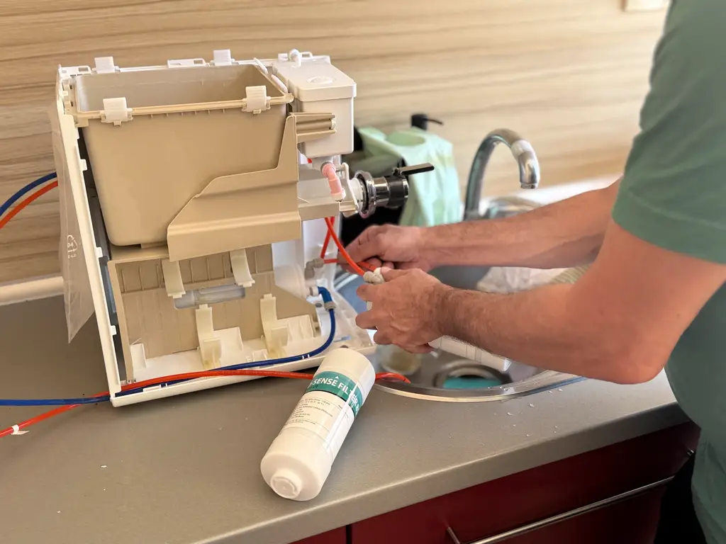 Technician repairing a refrigerator ice maker assembly at a kitchen counter